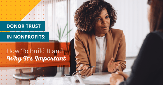 Photo of an African American woman with shoulder length brown curly hair wearing a tan blazer and white blouse. She is in a bright office sitting at a white desk holding a pen with papers in front of her. She is talking with a white woman with shoulder length straight brown hair and a black blazer facing away from the camera. Text to the left of the image says "Donor Trust in Nonprofits: How to Build it and Why It's Important."
