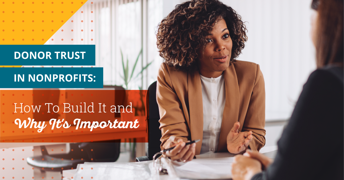 Photo of an African American woman with shoulder length brown curly hair wearing a tan blazer and white blouse. She is in a bright office sitting at a white desk holding a pen with papers in front of her. She is talking with a white woman with shoulder length straight brown hair and a black blazer facing away from the camera. Text to the left of the image says "Donor Trust in Nonprofits: How to Build it and Why It's Important."